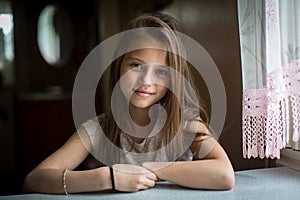 Cute ten-year-old girl posing for the camera sitting at the table.