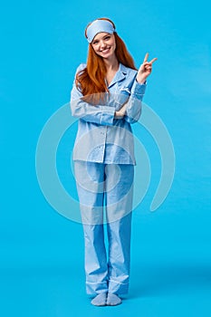 Cute and tender feminine lovely redhead woman in nightwear and sleep mask. Full length vertical studio shot ginger girl