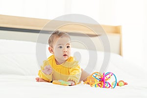 Cute thai newborn baby playing  funny in bed. Small baby in diaper lying on his belly on white bed with toys