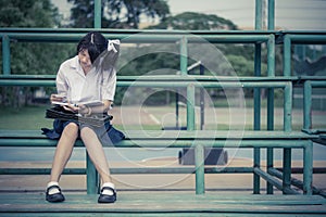 Cute Thai schoolgirl is sitting and reading on a stand in vintage color