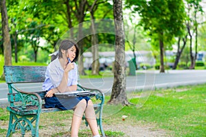 Cute Thai schoolgirl is sitting and studying on a bench