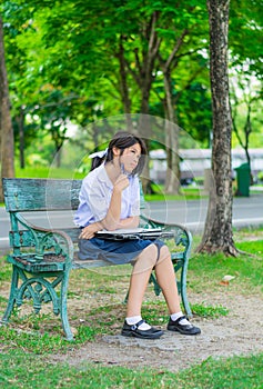 Cute Thai schoolgirl is studying and imagine something on a bench