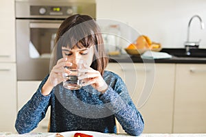 Cute thirsty girl drinking water in a glass at home