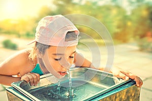 Cute thirsty girl drinks water from drinking sink