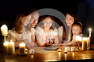 Cute thirteen years old girl making a wish before blowing candles on her birthday cake. Family of five celebrating childs birthday