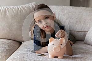 Cute thrifty little girl put coin into piggy bank