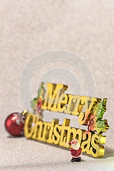 Cute tiny figurine of Santa Claus on a glitter silver snow background with the golden words Merry Christmas and a Christmas Tree