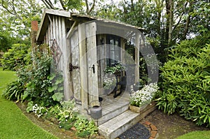 Cute tiny timber antique shack sitting in stunning flower garden