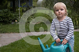 Cute toddler 2 years old girl with watering can in the garden at summer sunny day. Little child with garden tools in domestic