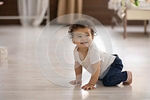 Cute toddler African American girl crawling on warm wooden floor