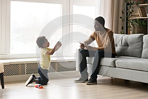 Cute toddler African American son showing toys to father