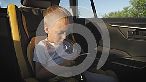 Cute toddler baby boy sitting in car seat and watching a video from smart-phone. Kid playing in the car with smartphone