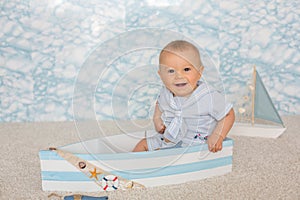 Cute toddler baby boy in wooden boat, playing with fishes, starfish and binoculars as sailman