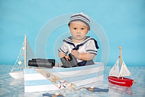 Cute toddler baby boy in wooden boat, playing with fishes, starfish and binoculars as sailman