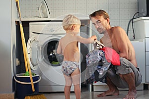 Cute toddler blond boy helps his father put the Laundry in the washing machine. Family housework, male housewife concept