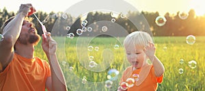 Cute toddler blond boy playing with soap bubbles on summer field. Happy child summertime concept. Authentic lifestyle image