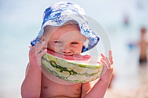 Cute toddler boy, blond child, eating watermelon on the beach coast