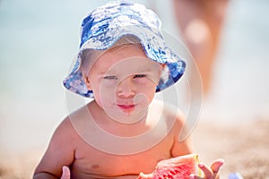 Cute toddler boy, blond child, eating watermelon on the beach coast