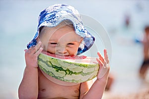 Cute toddler boy, blond child, eating watermelon on the beach coast