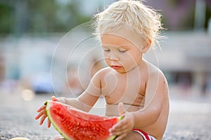 Cute toddler boy, blond child, eating watermelon on the beach coast