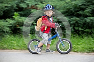 Cute toddler boy with blue helmet, riding balance bike on the street