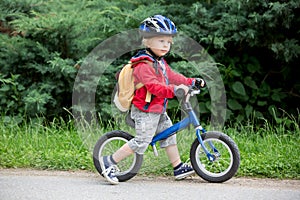 Cute toddler boy with blue helmet, riding balance bike on the street