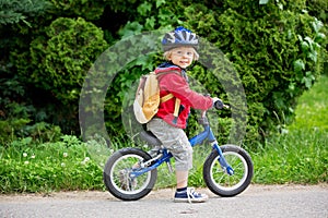 Cute toddler boy with blue helmet, riding balance bike on the street