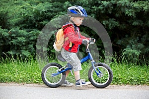 Cute toddler boy with blue helmet, riding balance bike on the street