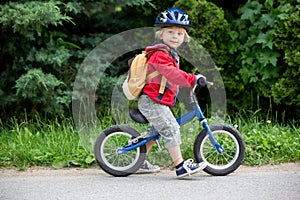 Cute toddler boy with blue helmet, riding balance bike on the street