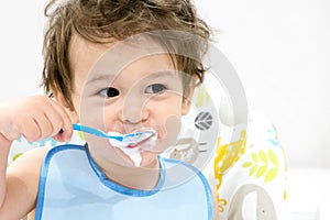 Cute toddler boy with blue spoon is yogurt. the child smiles. funny kid in a baby seat. beautiful 2 year old little boy eating Bre