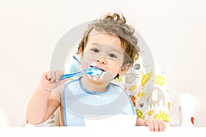 Cute toddler boy with blue spoon is yogurt. the child smiles. funny kid in a baby seat. beautiful 2 year old little boy eating Bre