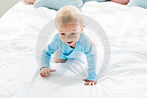 Cute toddler boy crawling on bed with white bedding at home