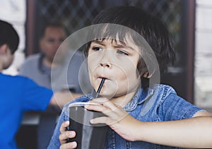 Cute toddler boy drinking cold drink, Happy Child sitting in cafe drinking soda or soft drink with a straw, Unhealthy drink for