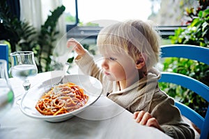 Cute toddler boy eating pasta in indoors restaurant