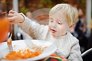 Cute toddler boy eating pasta in Italian indoors restaurant