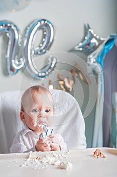 Cute toddler boy for first year of birth eating birthday cupcake with 1 candle close-up and copy space