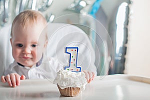 Cute toddler boy for first year of birth eating birthday cupcake with 1 candle close-up and copy space