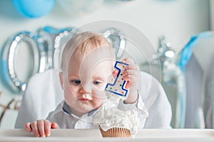 Cute toddler boy for first year of birth eating birthday cupcake with 1 candle close-up and copy space