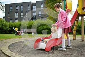 Cute toddler boy having fun with his big sister on a playground outdoors on warm autumn day