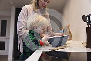 Cute toddler boy helping mum in the kitchen to bake a cake.