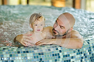 Cute toddler boy and his father having fun in indoor pool. Child learning to swim. Kid having fun with water toys. Family fun in a
