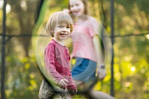Cute toddler boy and his sister jumping on a trampoline in a backyard. Sports and exercises for children