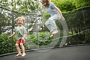 Cute toddler boy and his sister jumping on a trampoline in a backyard. Sports and exercises for children. Summer outdoor