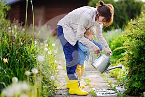 Cute toddler boy and his young mother watering plants in the garden