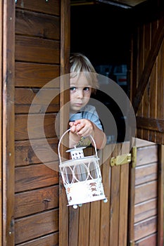 Cute toddler boy, holding lantern, hiding behind wooden door in little playhouse