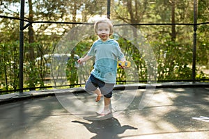 Cute toddler boy jumping on a trampoline in a backyard on warm and sunny summer day. Sports and exercises for children