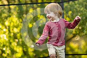 Cute toddler boy jumping on a trampoline in a backyard on warm and sunny summer day. Sports and exercises for children