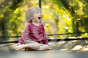 Cute toddler boy jumping on a trampoline in a backyard on warm and sunny summer day. Sports and exercises for children
