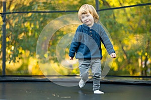 Cute toddler boy jumping on a trampoline in a backyard on warm and sunny summer day. Sports and exercises for children. Summer