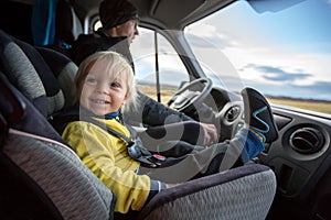 Cute toddler boy, kid sitting on the front seat in child seat on big camper van, smiling